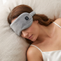 Woman wearing a gray sleep mask while lying on a pillow.
